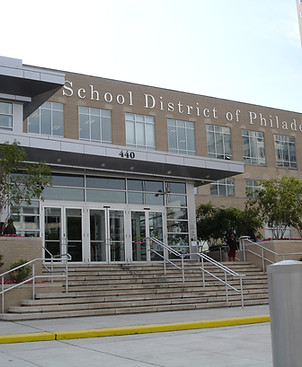 Image shows the exterior of the main School District of Philadelphia office, it is a two story brick and metal building with large windowed doors in the front. Photo credit: Its Our City